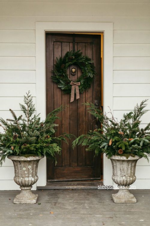 Greenery filled stone urns framing a christmas farmhouse front door