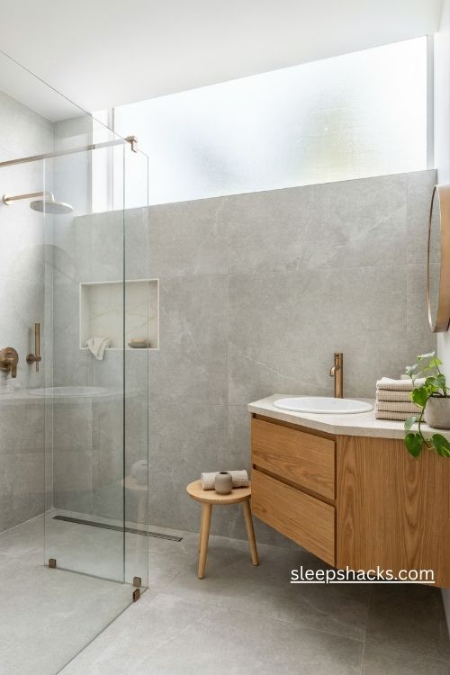  Grey bathroom with frameless glass shower enclosure recessed niche and brass rainfall shower head