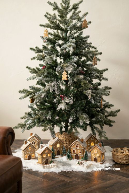 Miniature glowing gingerbread village under a Christmas tree on a snowy blanket in a cozy living room