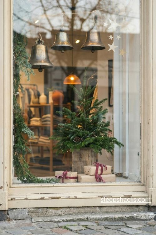 Minimalist christmas storefront display with vintage brass bells evergreen branches and warm boutique window lighting