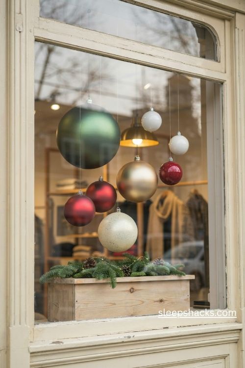 Oversized christmas ornaments hanging at different heights in an elegant boutique storefront window