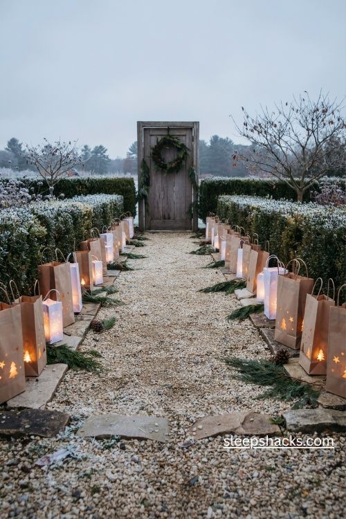 Paper bag luminaries with glowing star and snowflake cutouts lining a rustic Christmas walkway