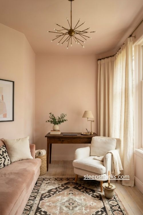 Pastel pink home office with white armchair patterned rug and elegant chandelier