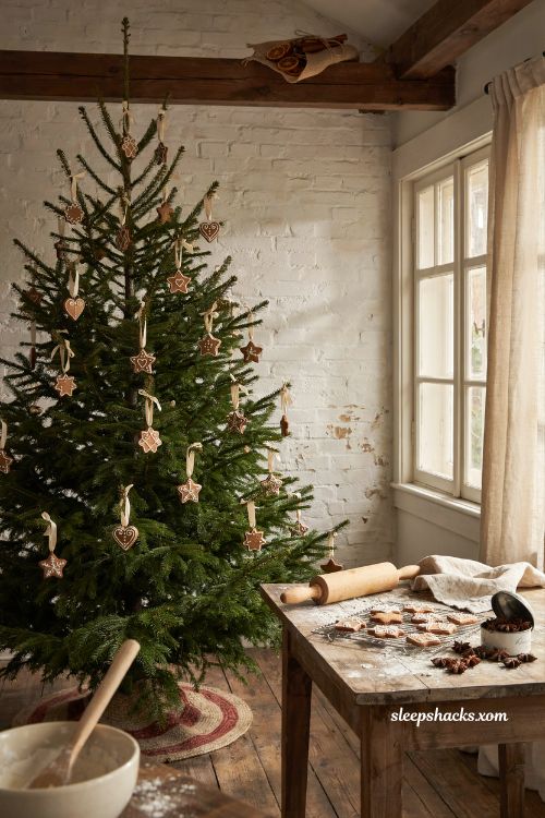 Real baked gingerbread cookie ornaments hanging on a rustic Christmas tree in a cozy kitchen