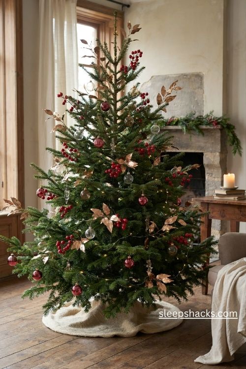 Red berry picks and gold leaves on a natural christmas tree with simple glass ornaments