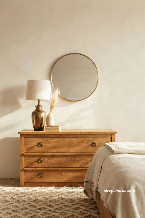 Round brushed brass mirror and cream bedroom dresser with warm lighting