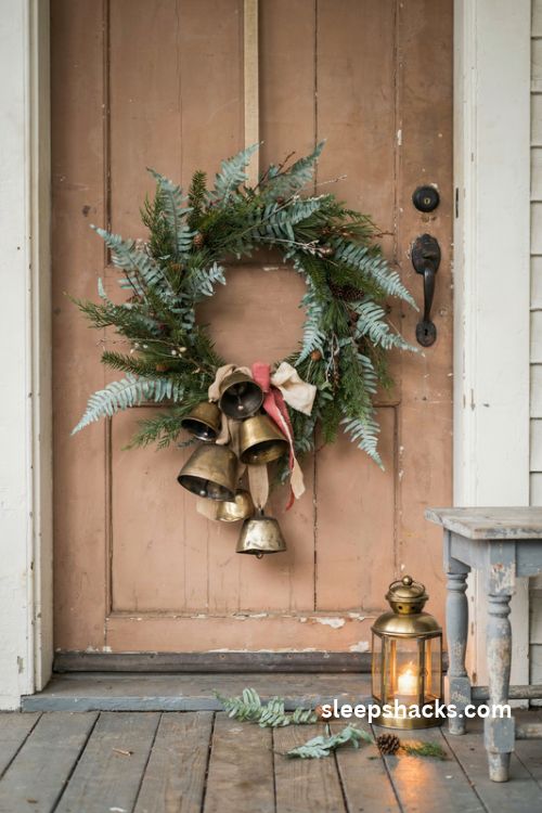 Rustic christmas wreath with antique brass jingle bells fern greenery and a muted red ribbon on a farmhouse door