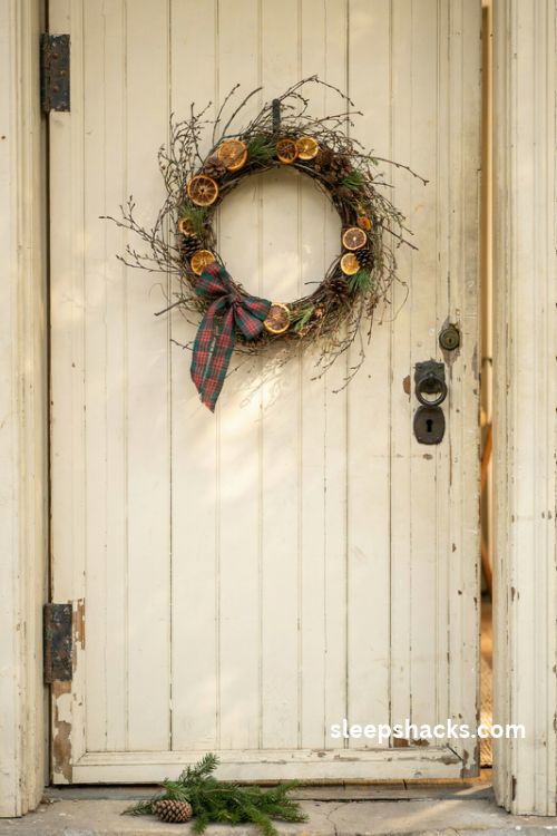 Rustic christmas wreath with dried orange slices twigs and plaid ribbon on a farmhouse door