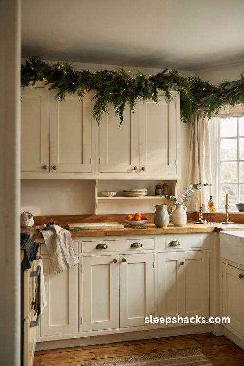 Small kitchen Christmas garland above cabinets with warm white fairy lights and greenery