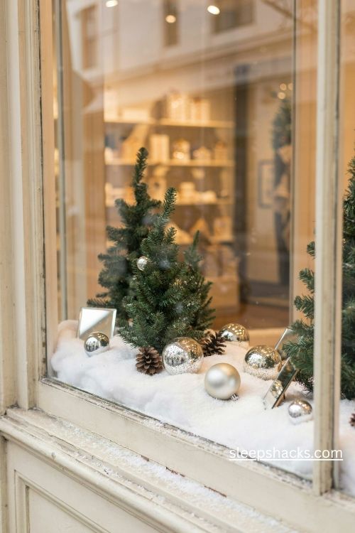 Snowy christmas storefront window with sparkling faux snow silver ornaments mirrored accents and warm holiday lights