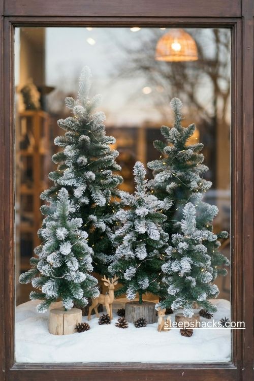 Snowy forest christmas storefront display with white flocked trees faux snow pinecones and warm lights