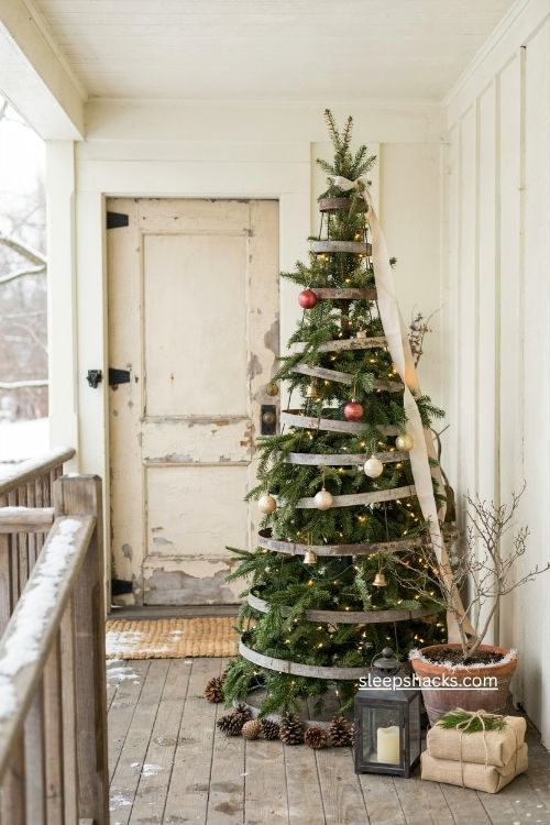 Tomato cage christmas tree wrapped in garland and lights with pinecones on a rustic front porch 