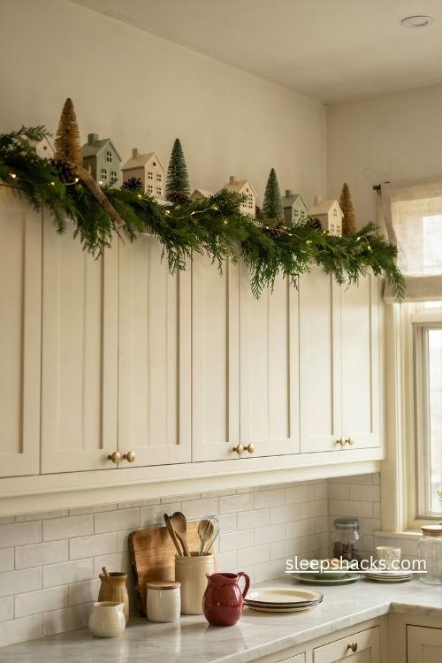 Top of cabinet christmas decor with evergreen garland vintage houses bottle brush trees and warm fairy lights