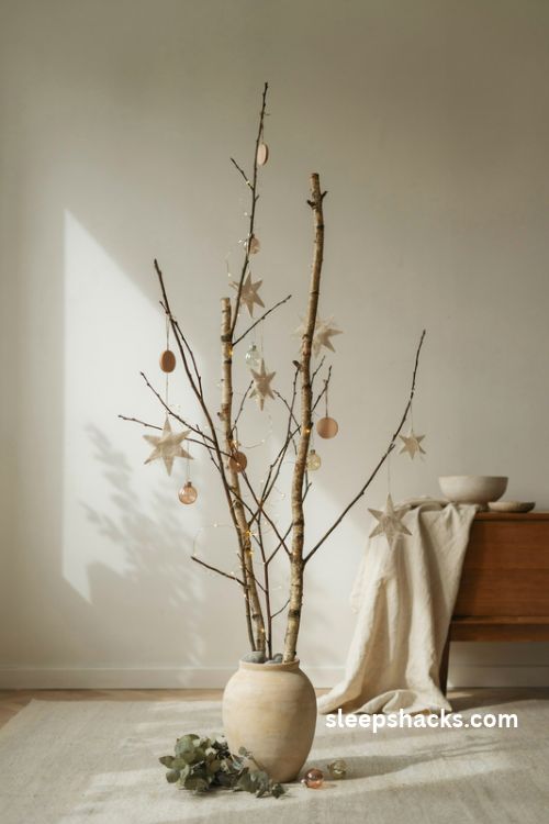 Twig christmas tree in a ceramic vase with paper stars wooden ornaments and warm fairy lights