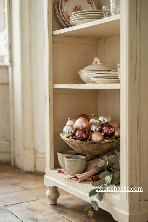 Vintage christmas ornaments in bowls and ironstone dishes on a cozy christmas hutch