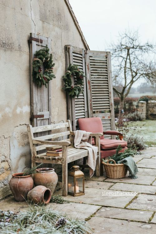 Vintage cottage Christmas courtyard with weathered bench old shutters wreaths and lantern 