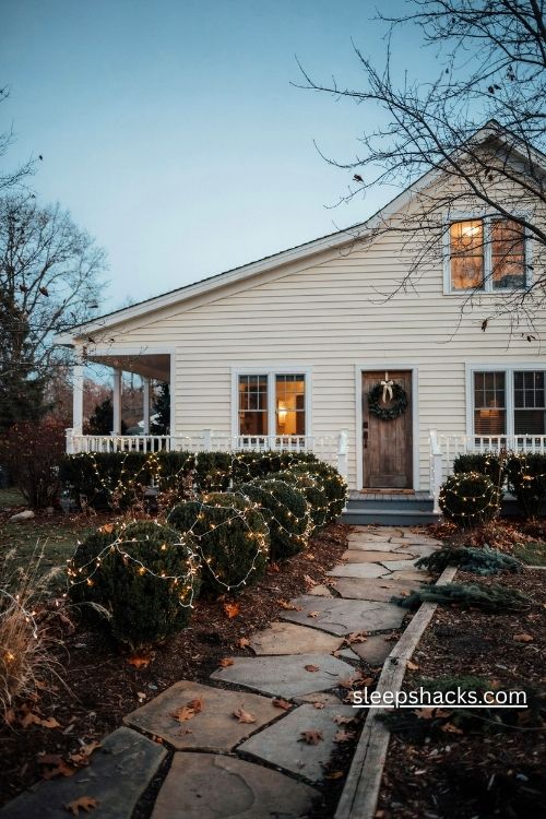 Warm white net lights covering evergreen shrubs and hedges in a cozy christmas front yard