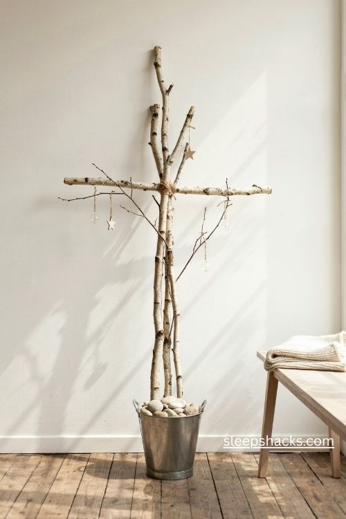 White birch branch cross christmas tree with silver ornaments and paper stars beside a window