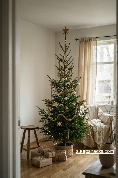 Wooden bead garland on a slim pencil christmas tree with white ornaments and handmade paper stars