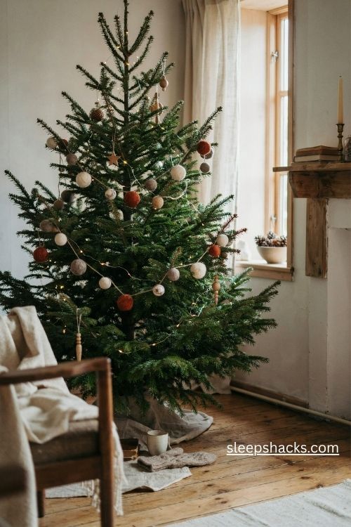 Wool pom pom christmas garland in cream rust and forest green draped around a natural evergreen tree