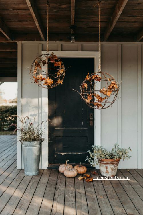 fall porch with hanging bronze wire spheres and dried leaves by black front door 