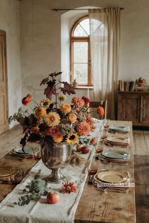 lush fall floral centerpiece with orange yellow blooms and purple foliage in silver urn 