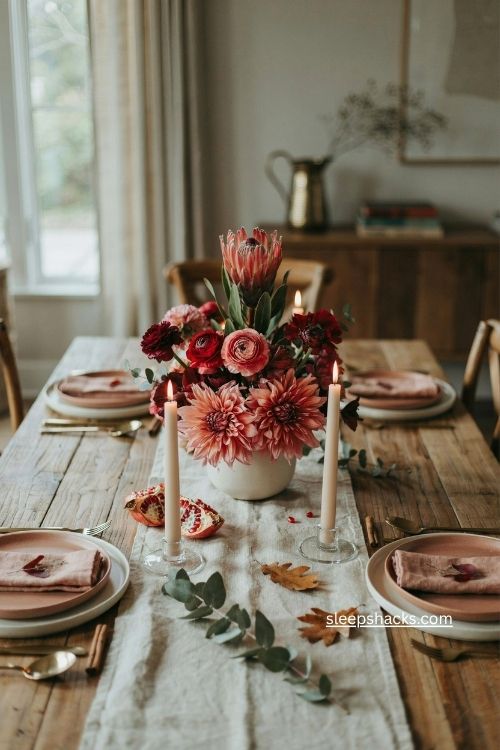 red thanksgiving floral centerpiece with protea ranunculus dahlias and tapered candles 