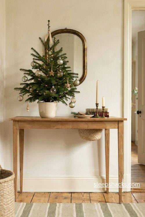 small tabletop christmas tree on a vintage console table with candles, books, and cozy entryway decor